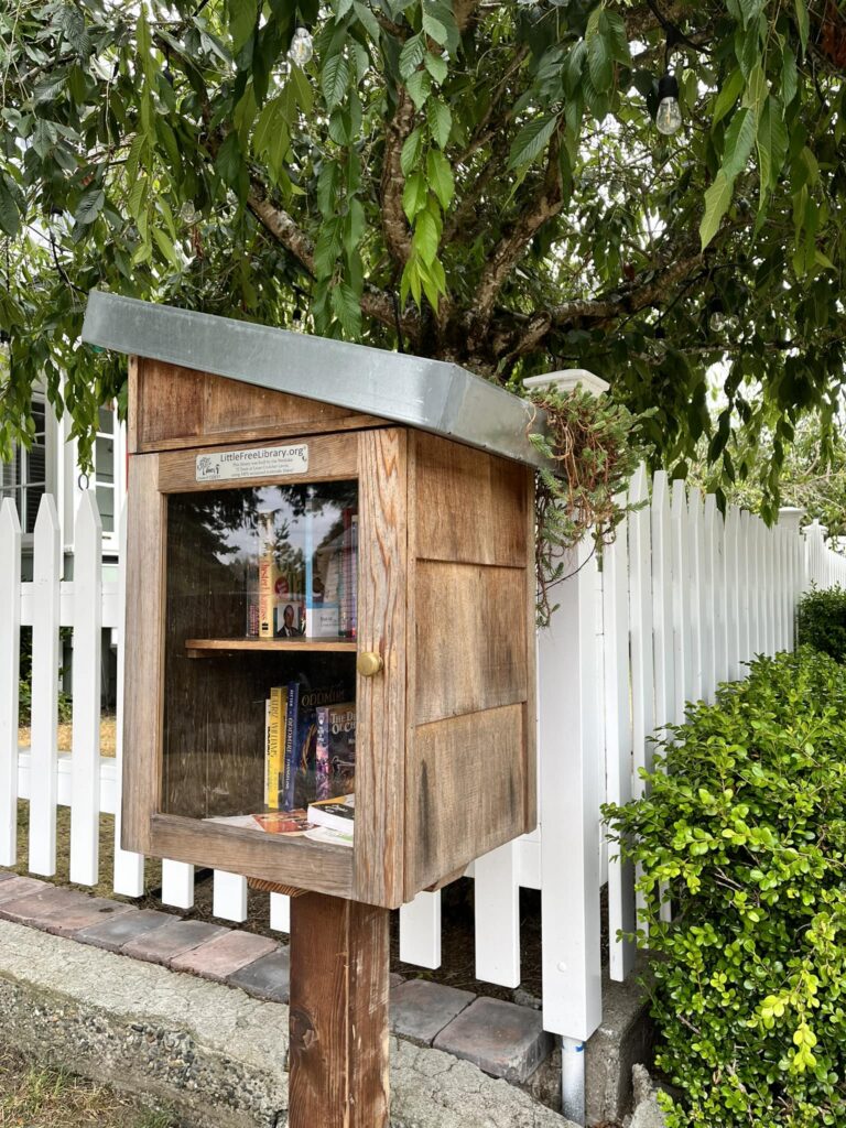 A brown wooden Little Free Library with an angled metal roof. 