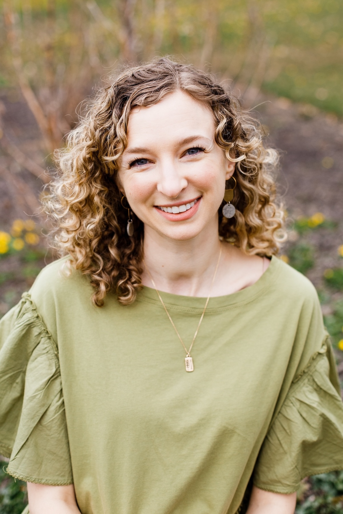 A smiling white woman with curly blonde hair, wearing a light green shirt. 